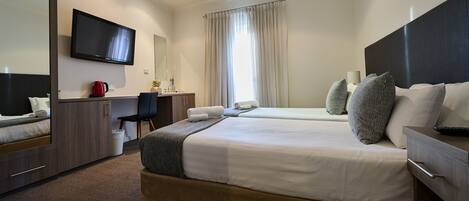 Habitación de hotel con cama, escritorio, silla, televisor y ventilador de techo.