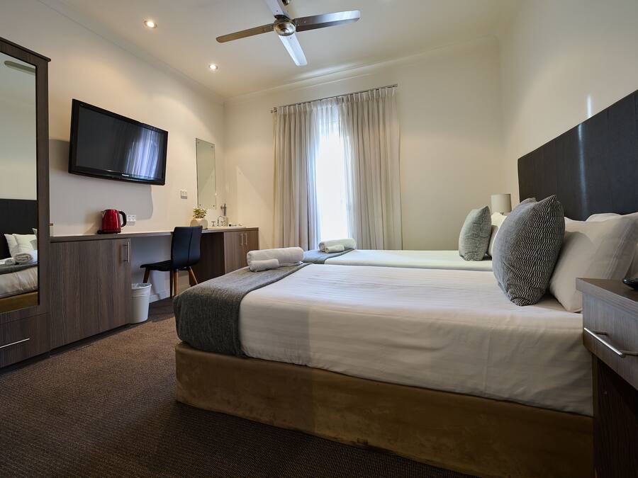 Een hotelkamer met een bed, een bureau, een stoel, een televisie en een plafondventilator.