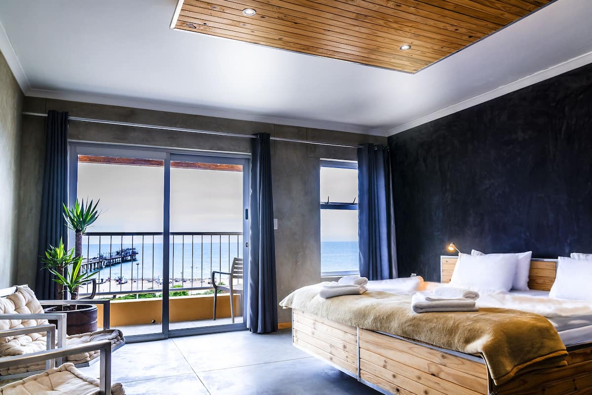 Una habitación de hotel moderna con una cama grande, un balcón con vistas al mar y un techo de madera.