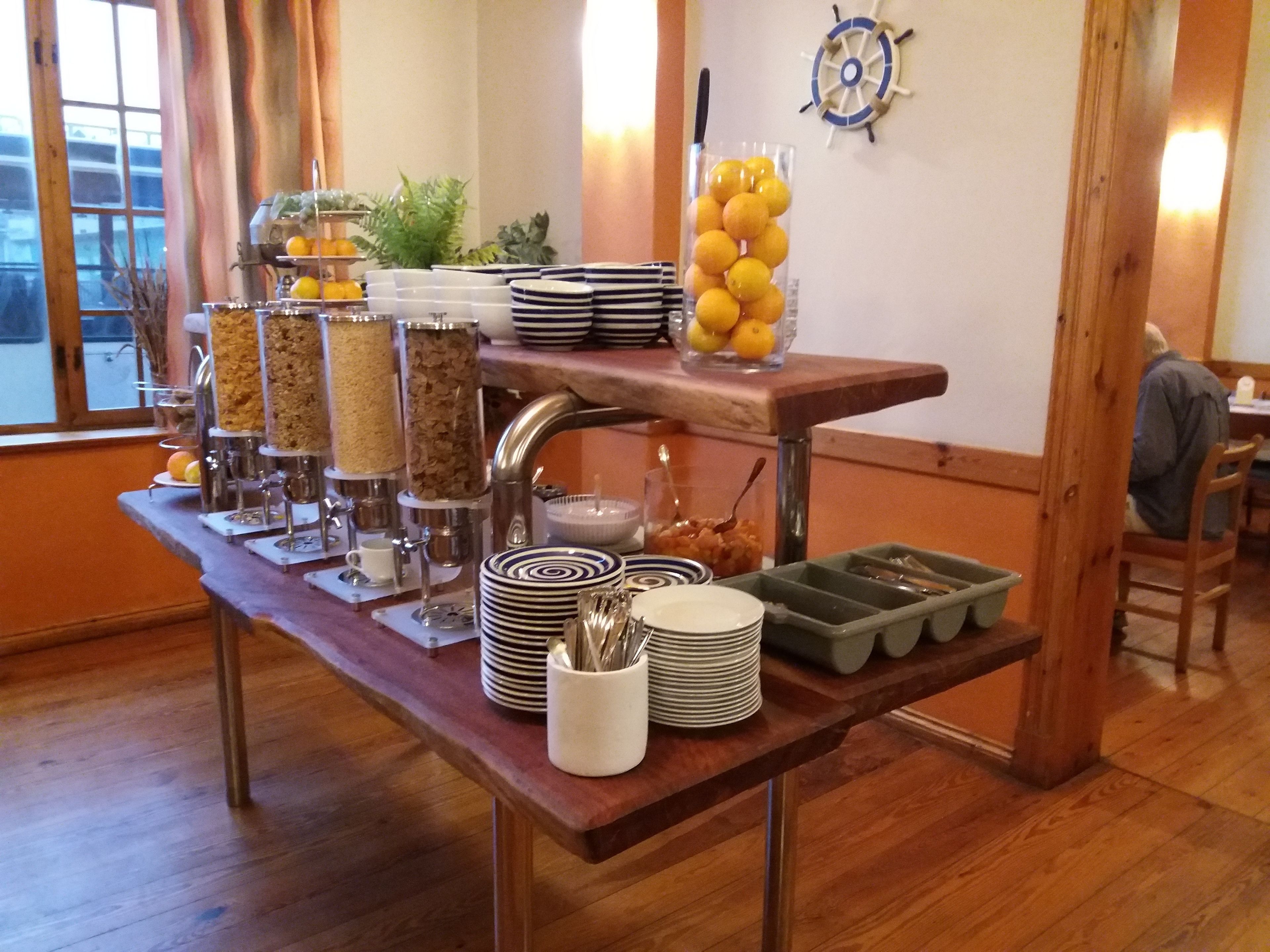A buffet setup with various food items and utensils, a ship wheel decoration on the wall, and a window view.