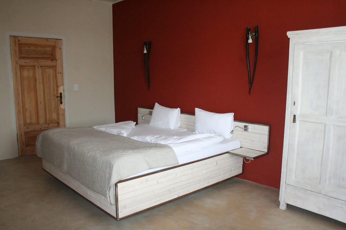Un dormitorio con cama de madera, ropa de cama blanca, una pared de acento roja y un armario blanco.