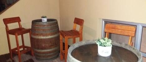 A room with a wooden floor, two wooden chairs, a round wooden table with a potted plant, and two wooden barrels.