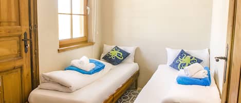 A small, clean room with two single beds, a window, and wooden doors.
