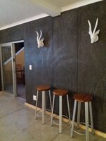 Una habitación con una pared oscura y texturizada, tres taburetes de madera y una puerta blanca que da a otra estancia.