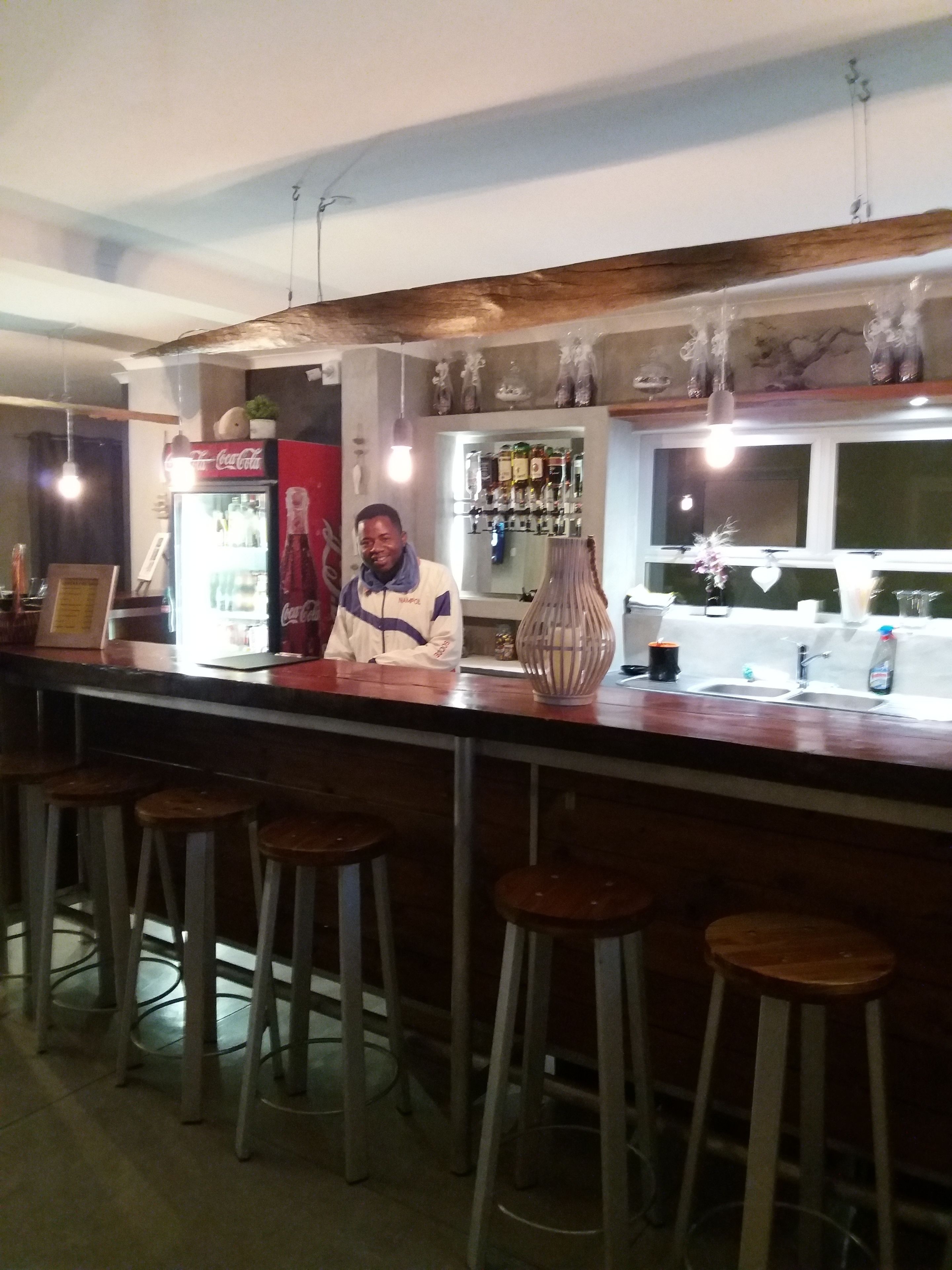 Una zona de bar con taburetes, un refrigerador y estantes con botellas.