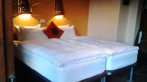 Una cama doble con sábanas blancas, un cojín decorativo rojo y dos lámparas fijadas a la pared.