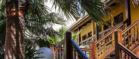 A staircase with wooden railings leading to a building with multiple windows and a palm tree nearby.