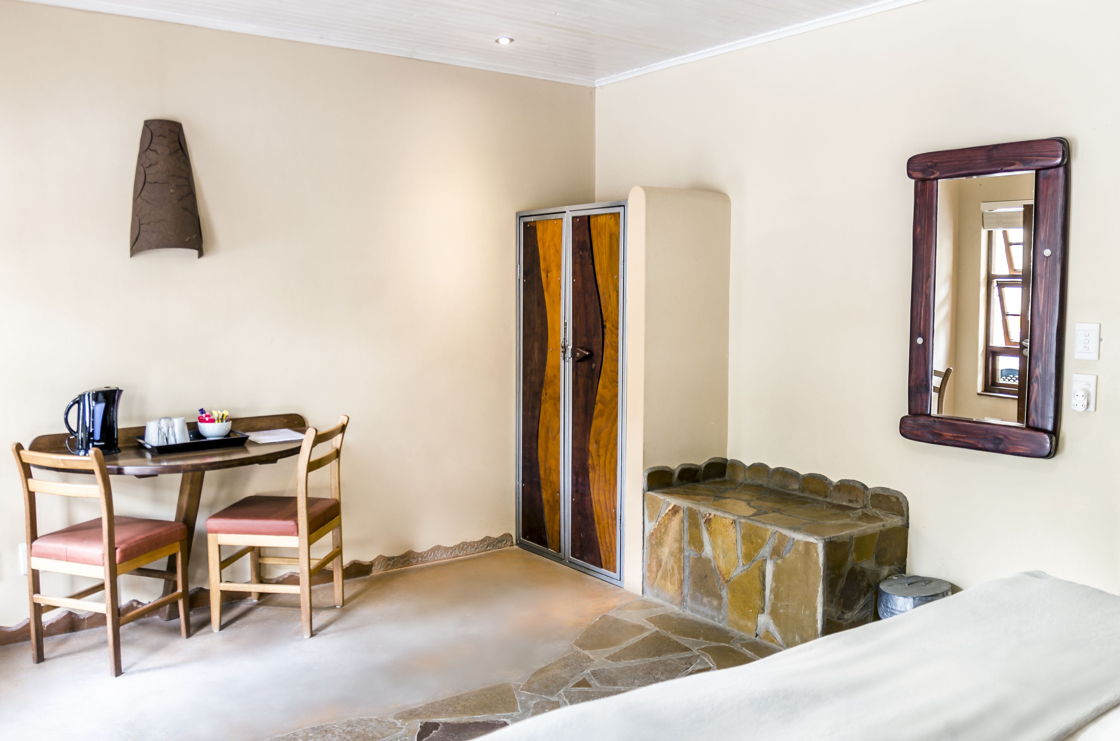 Une pièce comprenant un lit, une cheminée en pierre, une table en bois avec des chaises, une armoire en bois et un miroir au mur.