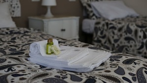 A neatly made bed with a patterned bedspread, a folded white towel, and two small bottles of lotion on the bed. - My Sweet Rome (Rome)