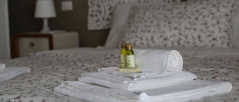 A neatly made bed with folded white towels and two bottles of olive oil on the bed.