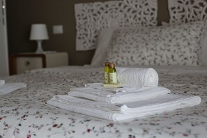 A neatly made bed with folded white towels and two bottles of olive oil on the bed. - My Sweet Rome (Rome)