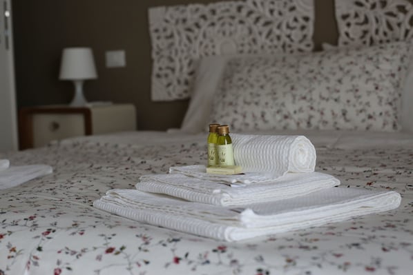 A neatly made bed with folded white towels and two bottles of olive oil on the bed. - My Sweet Rome (Rome)