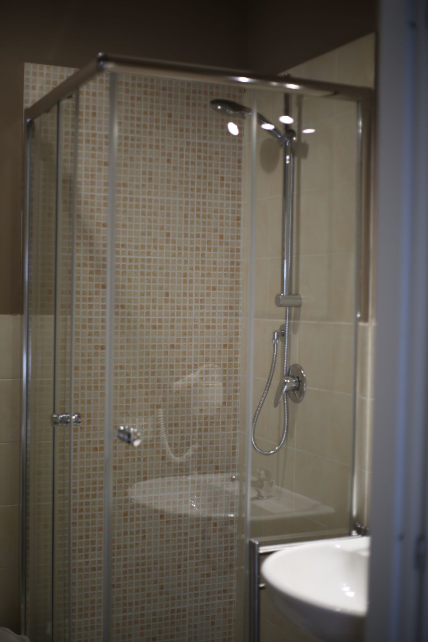 A glass-enclosed shower with a tiled wall, a sink, and a showerhead.