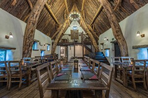 Una larga mesa de comedor con sillas de madera, techo de madera y una escalera que sube a un nivel superior.