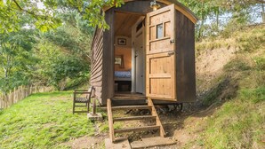 A wooden cabin with a single bed, a small window, and a door. - Craven Shepherd Huts (Skipton)