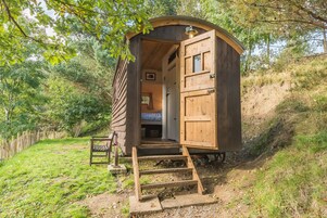 Una cabaña de madera con una cama individual, una ventana pequeña y una puerta.
