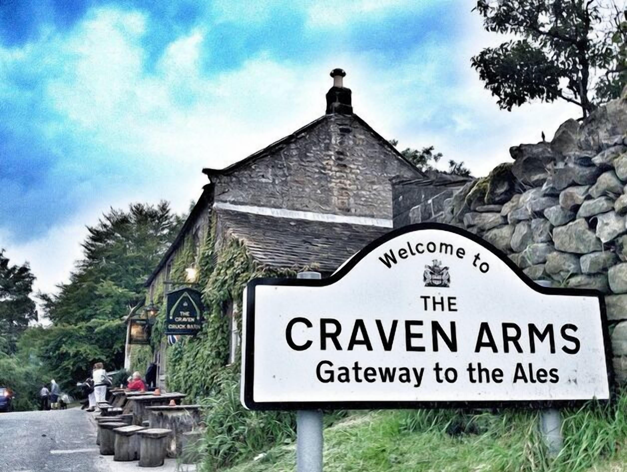 A sign welcoming visitors to Craven Arms, a pub with a stone facade and ivy-covered walls.