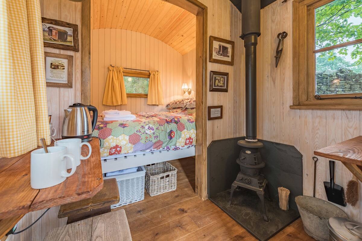 Una habitación acogedora con una cama, una mesa de madera con tazas, una tetera y un estufa de leña.