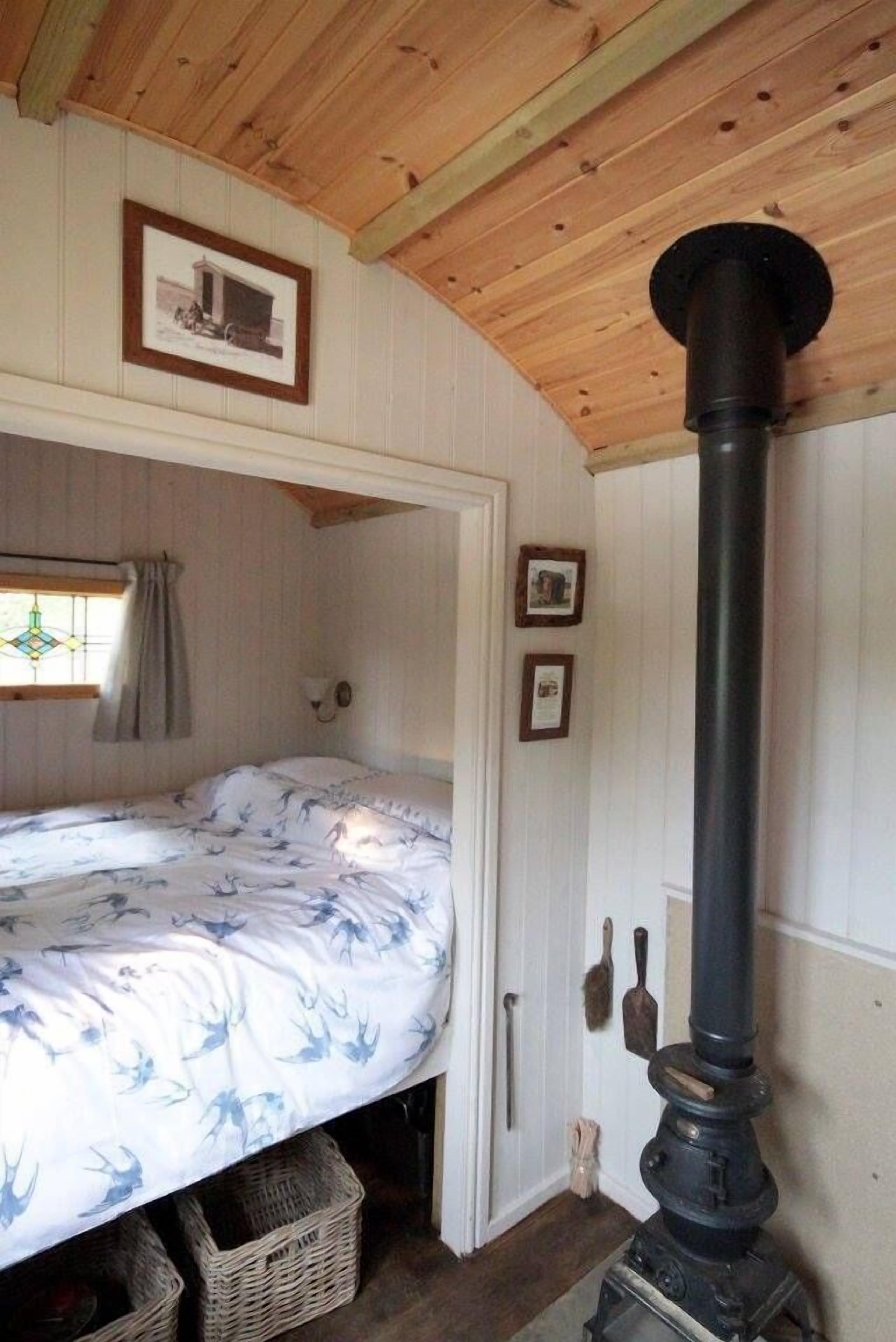 Una stanza accogliente con un letto, un soffitto in legno, un fornello nero e quadri appesi al muro.