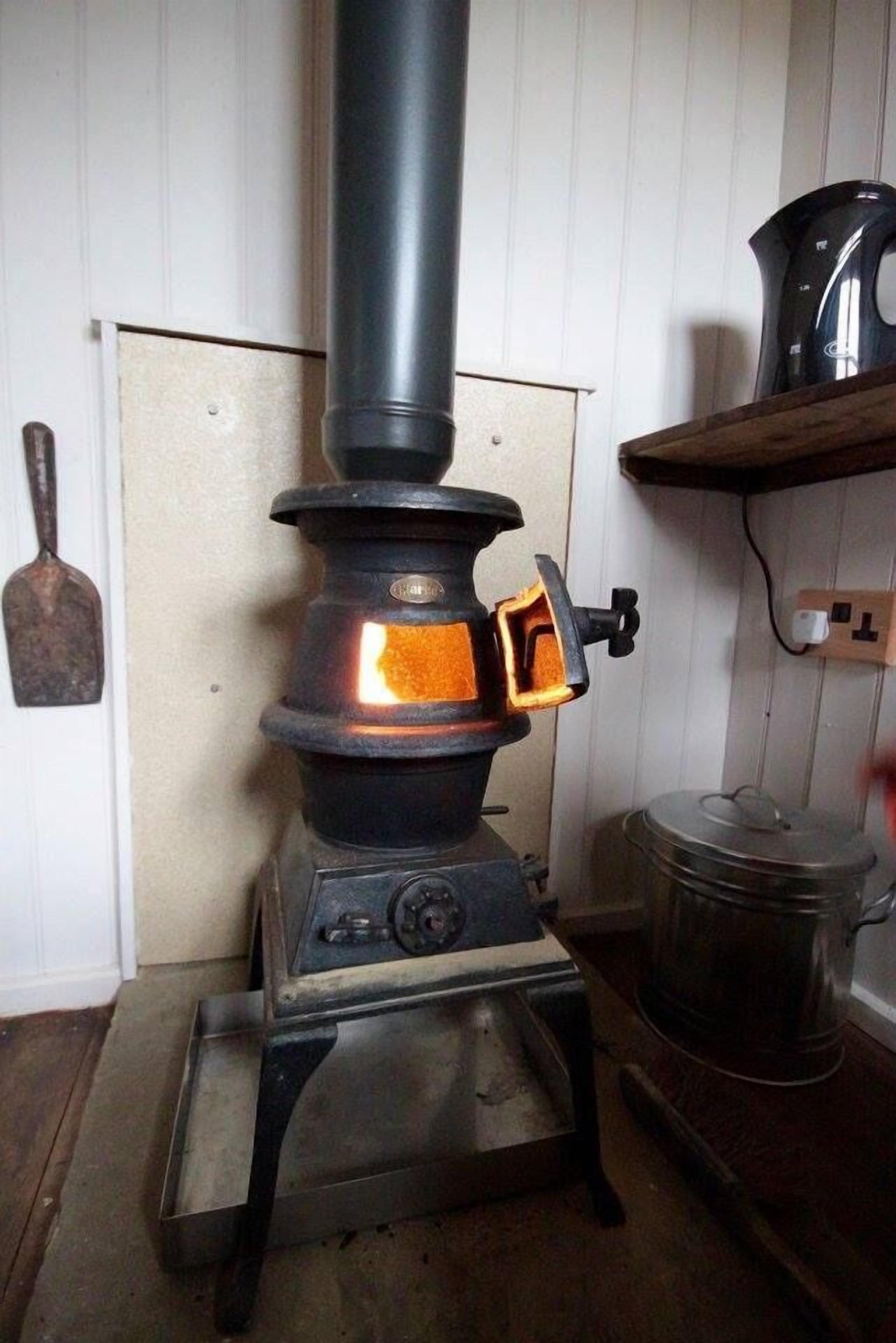 A wood-burning stove with a chimney, a pot on the stove, and a shovel on the wall.