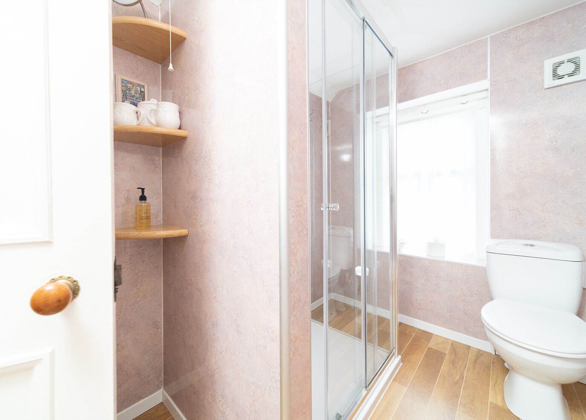 Un baño con cabina de ducha de vidrio, inodoro y estantes de madera con artículos de aseo.