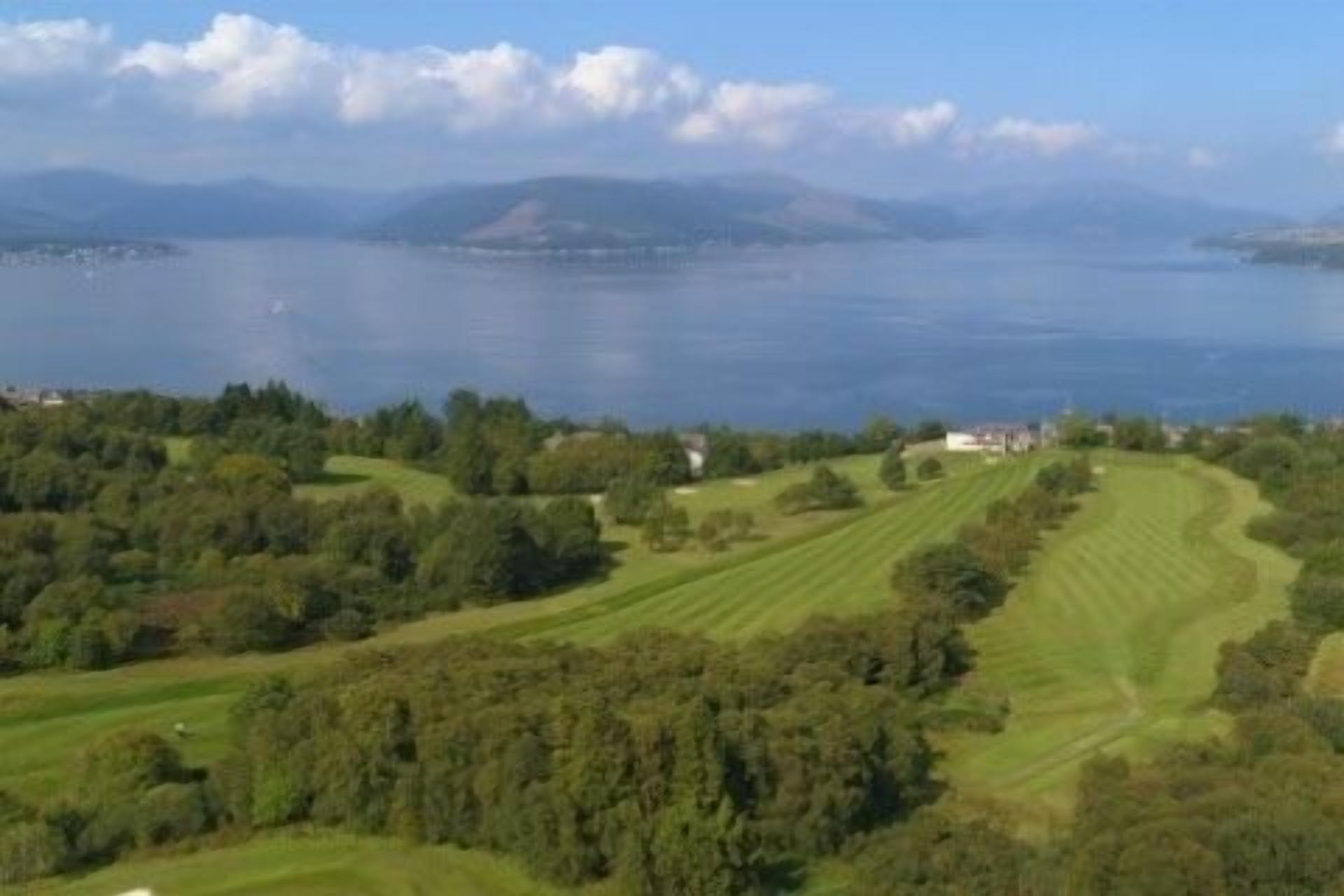 Un parcours de golf offrant une vue sur un lac et des montagnes lointaines.