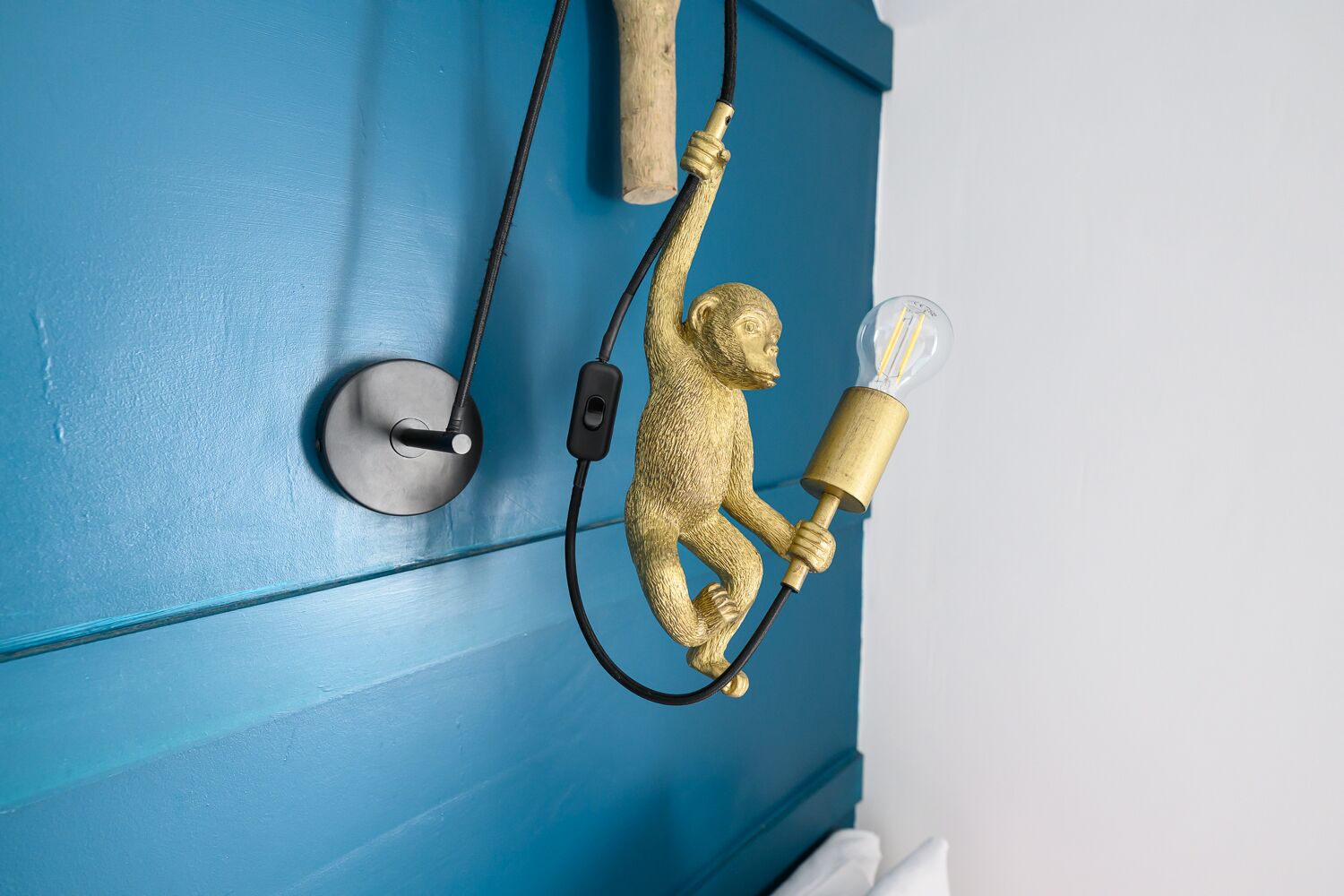 Un luminaire mural représentant un singe tenant une lampe, et raccordé à une source d’alimentation.