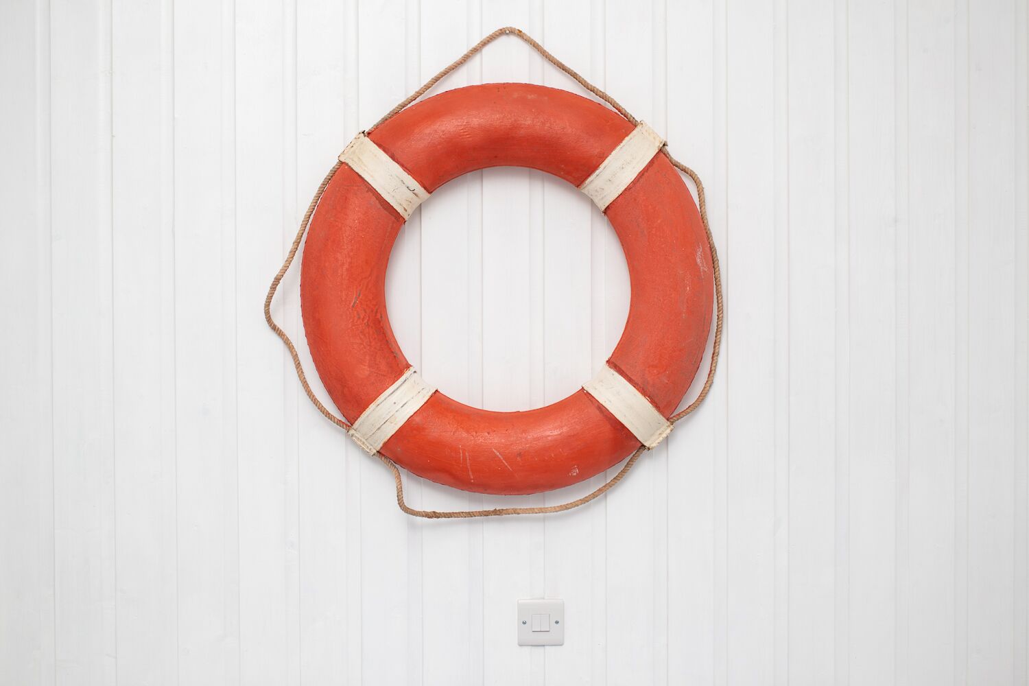 Une bouée de sauvetage rouge avec des sangles blanches, suspendue à un mur blanc.
