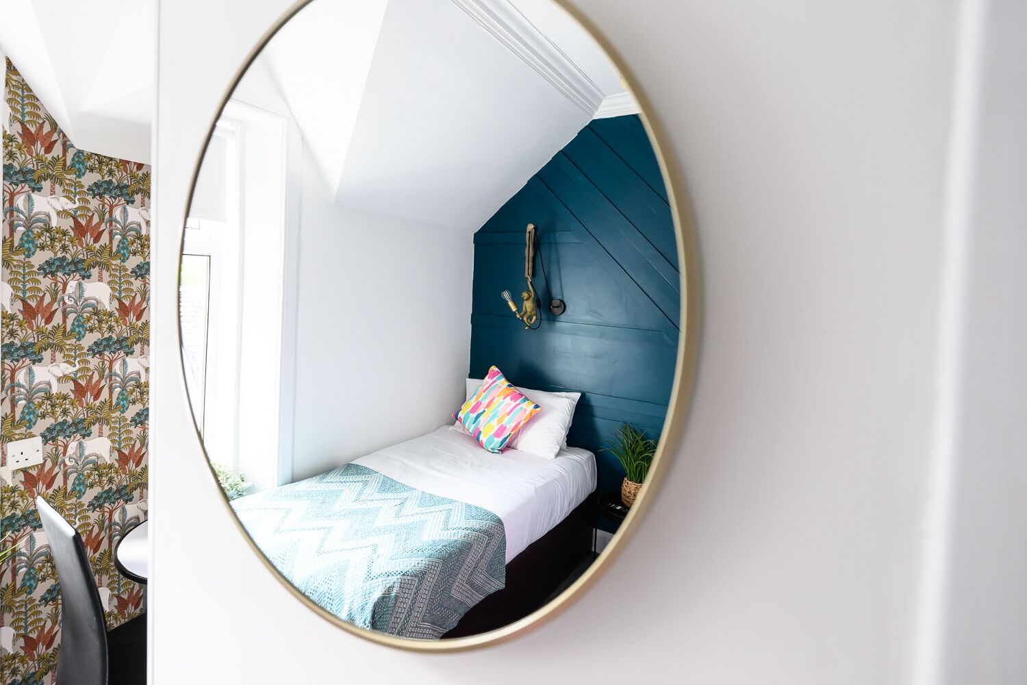 A bedroom with a bed, a mirror, and a wall with a patterned wallpaper.