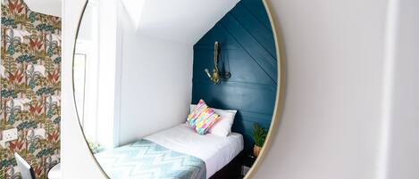 A bedroom with a bed, a mirror, and a wall with a patterned wallpaper.