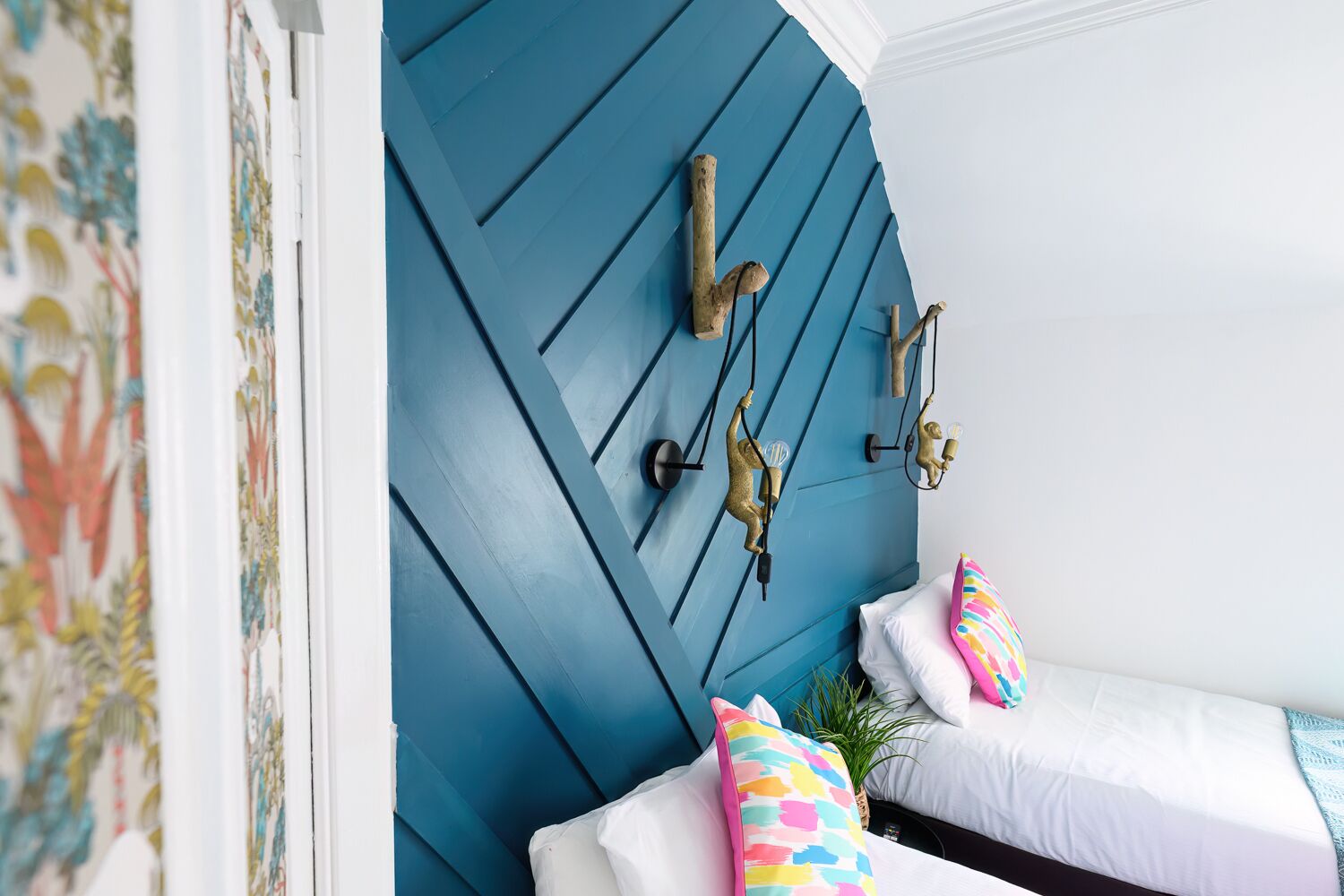 Ein Schlafzimmer mit blauer Akzentwand, einem Bett mit weißer Bettwäsche und farbenfrohen Kissen.