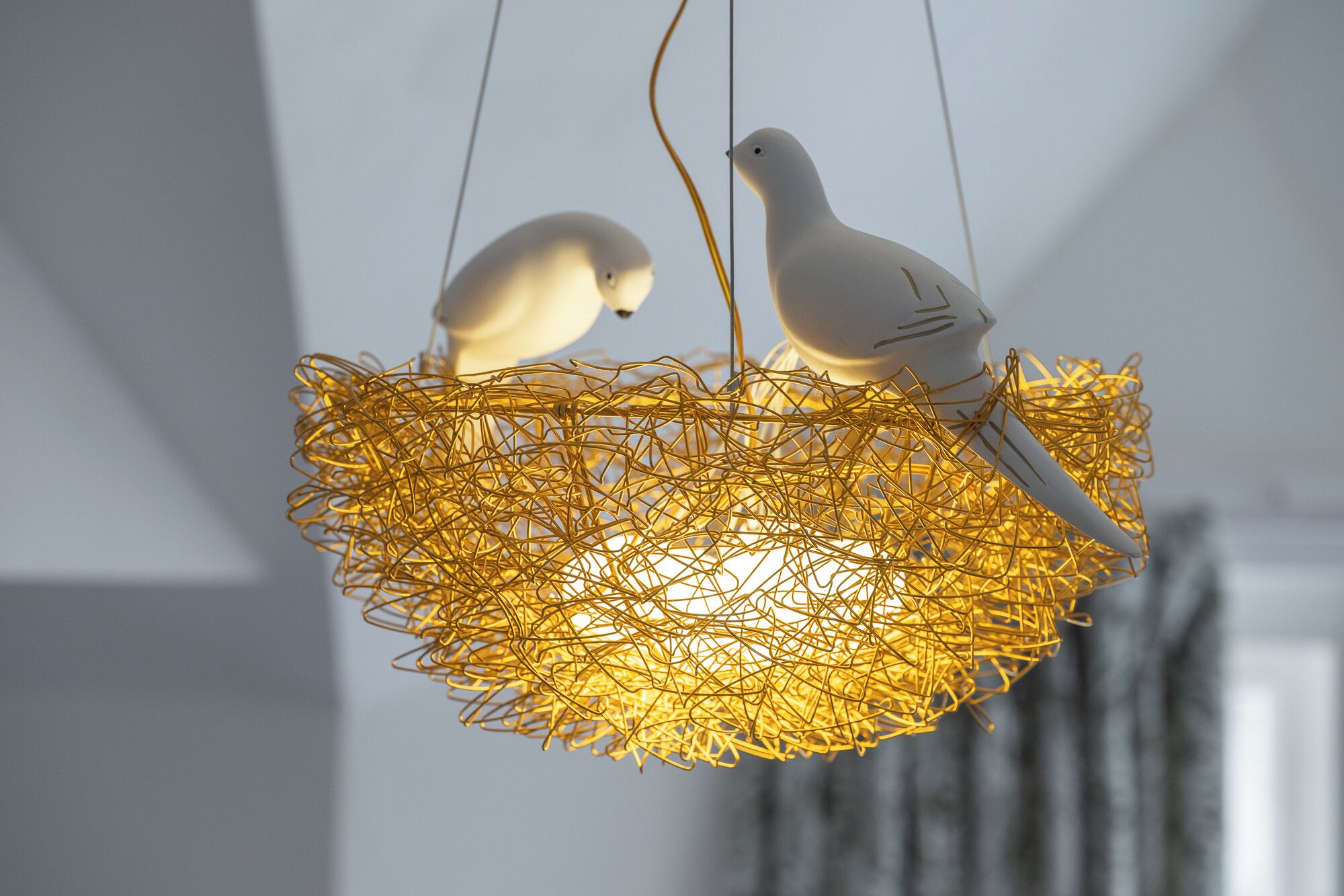 Dos aves blancas posadas en una lámpara colgante hecha de alambres dorados entrelazados.