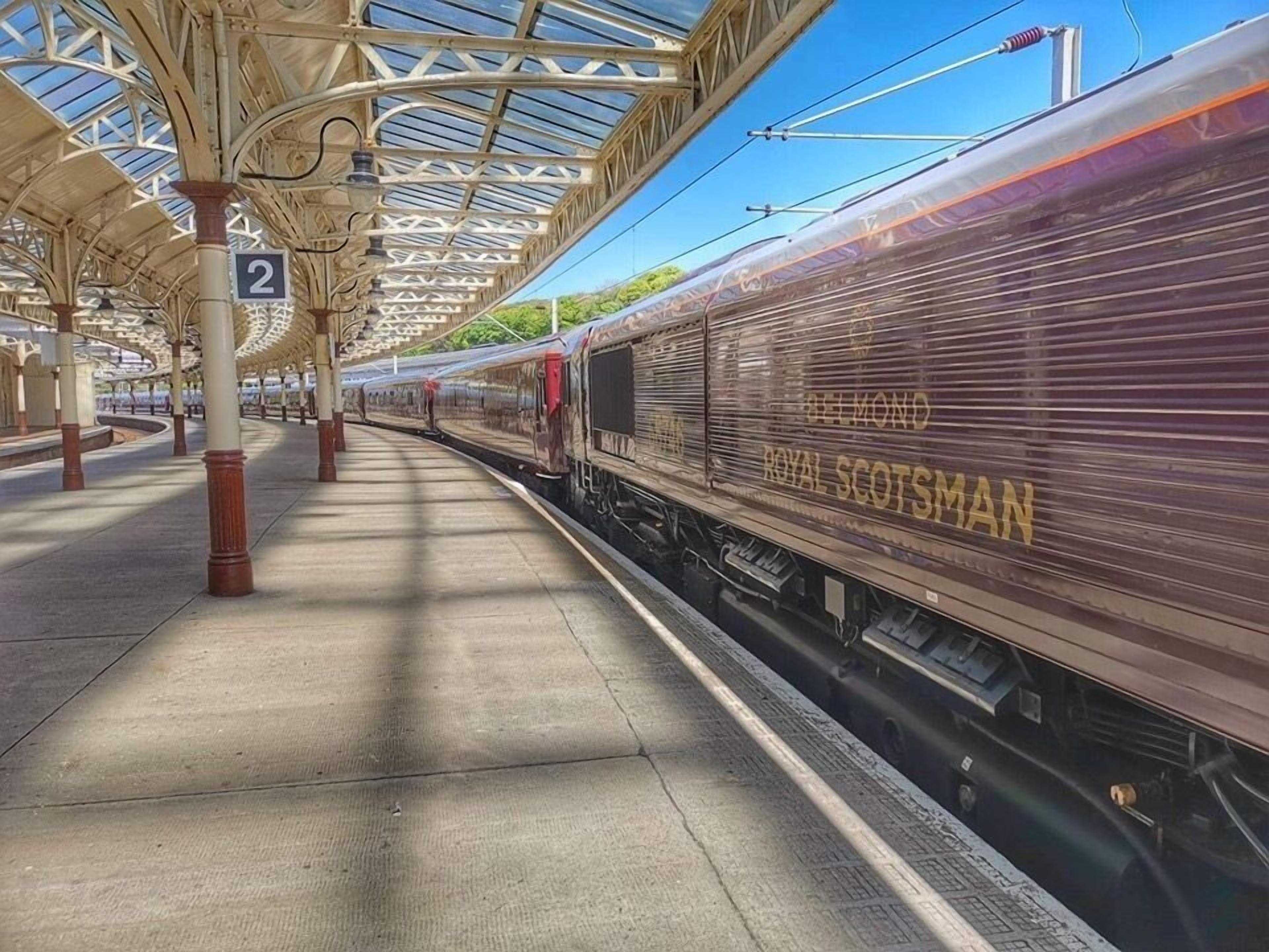 Un andén de estación de tren con techo cubierto y un tren identificado como "Royal Scotman".