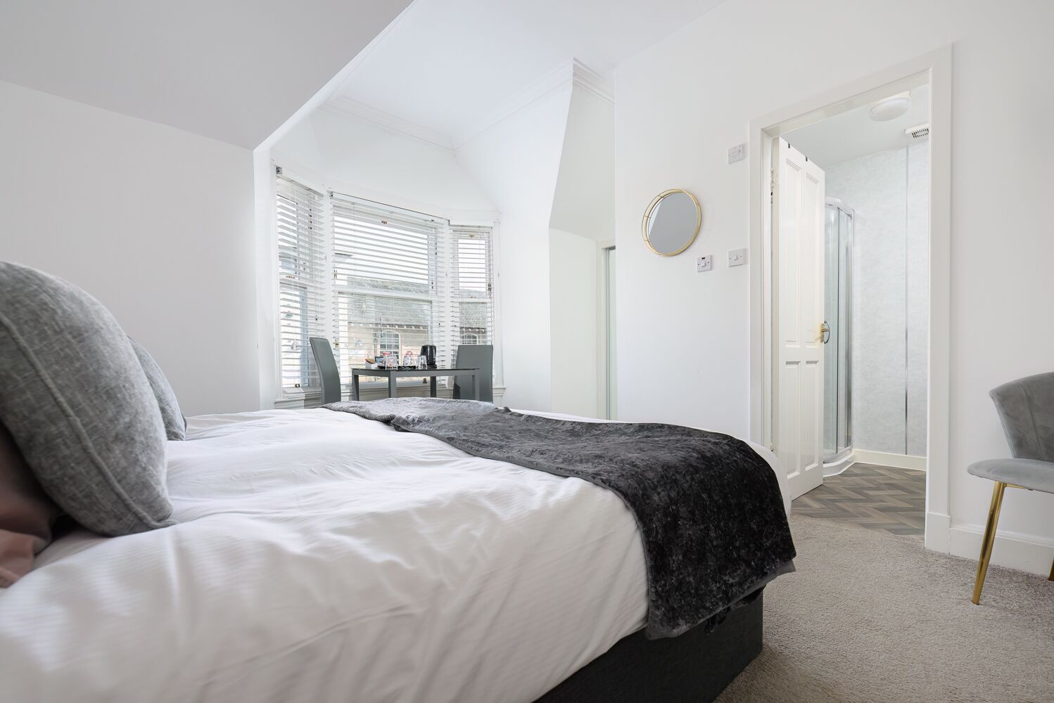 Une chambre moderne avec un lit, un bureau et une chaise. Une porte donne accès à une salle de bain.