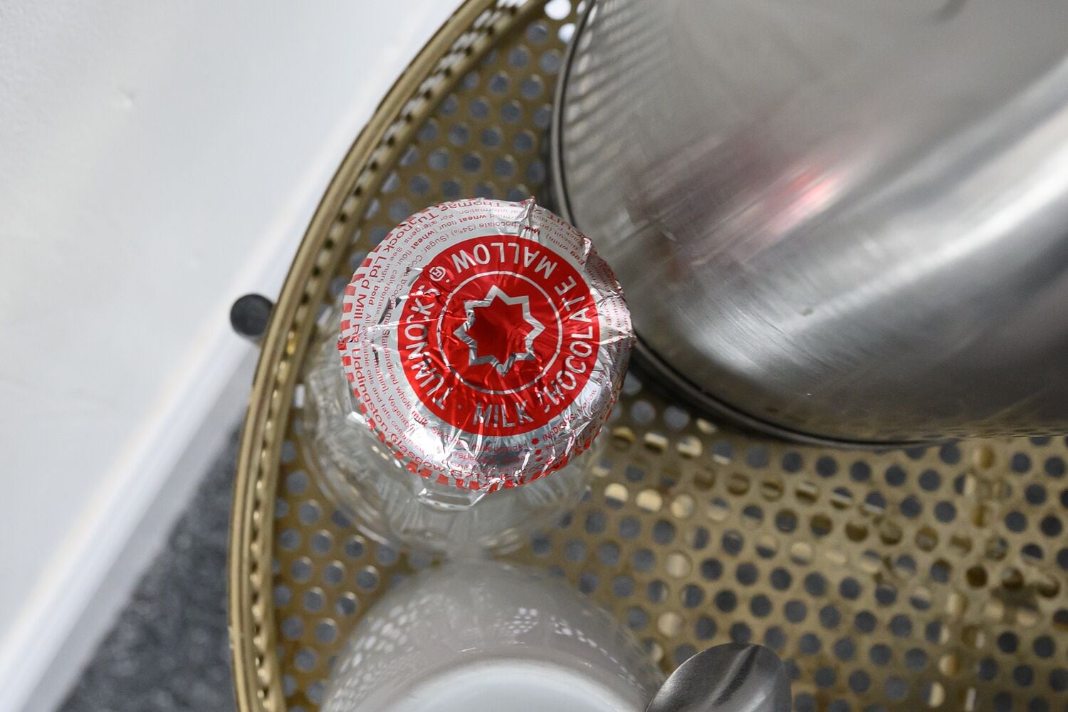 A bottle of milk chocolate in a clear plastic bottle with a red label, placed on a perforated tray.