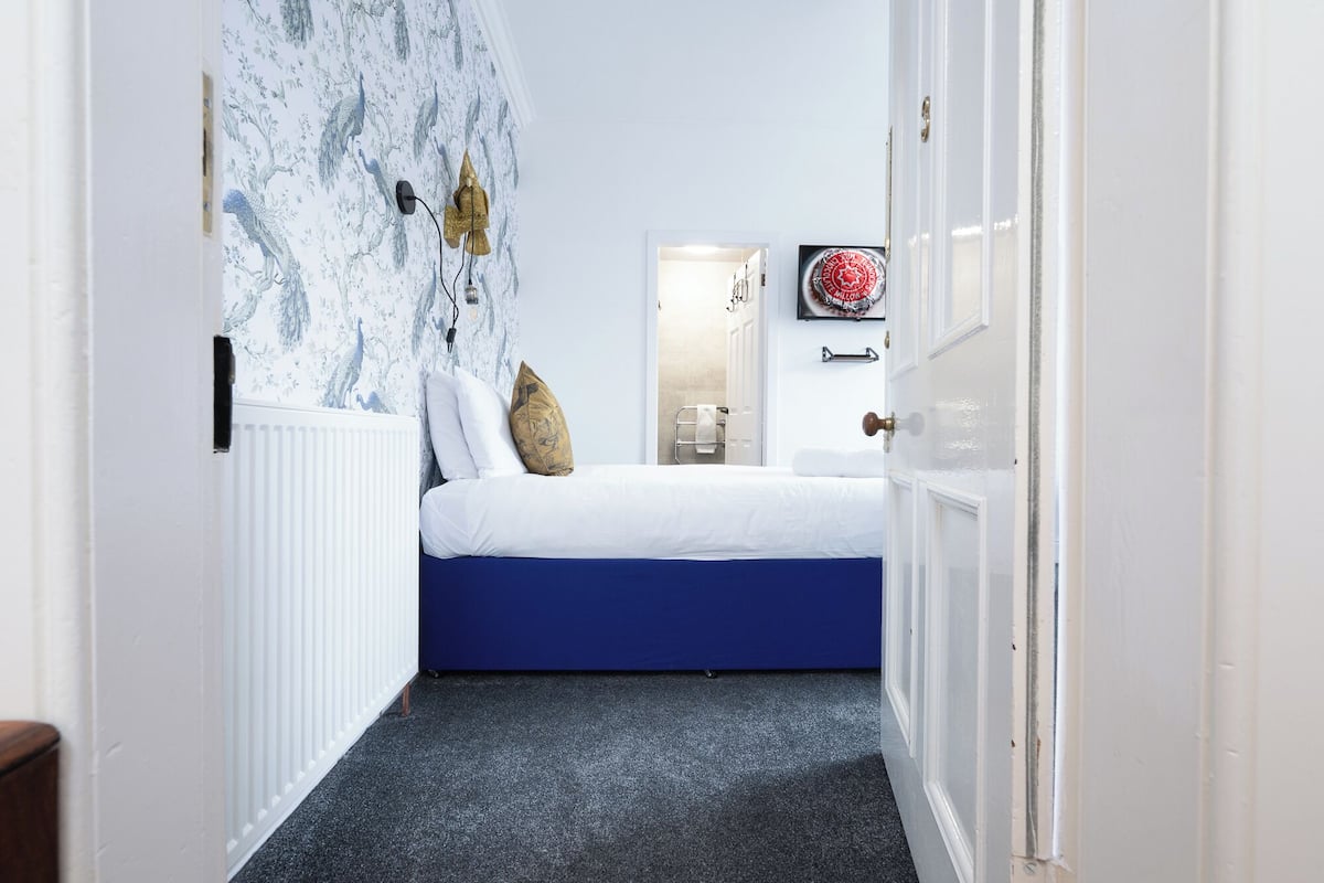 A bedroom with a blue bed, white bedding, and a wall with a bird pattern.
