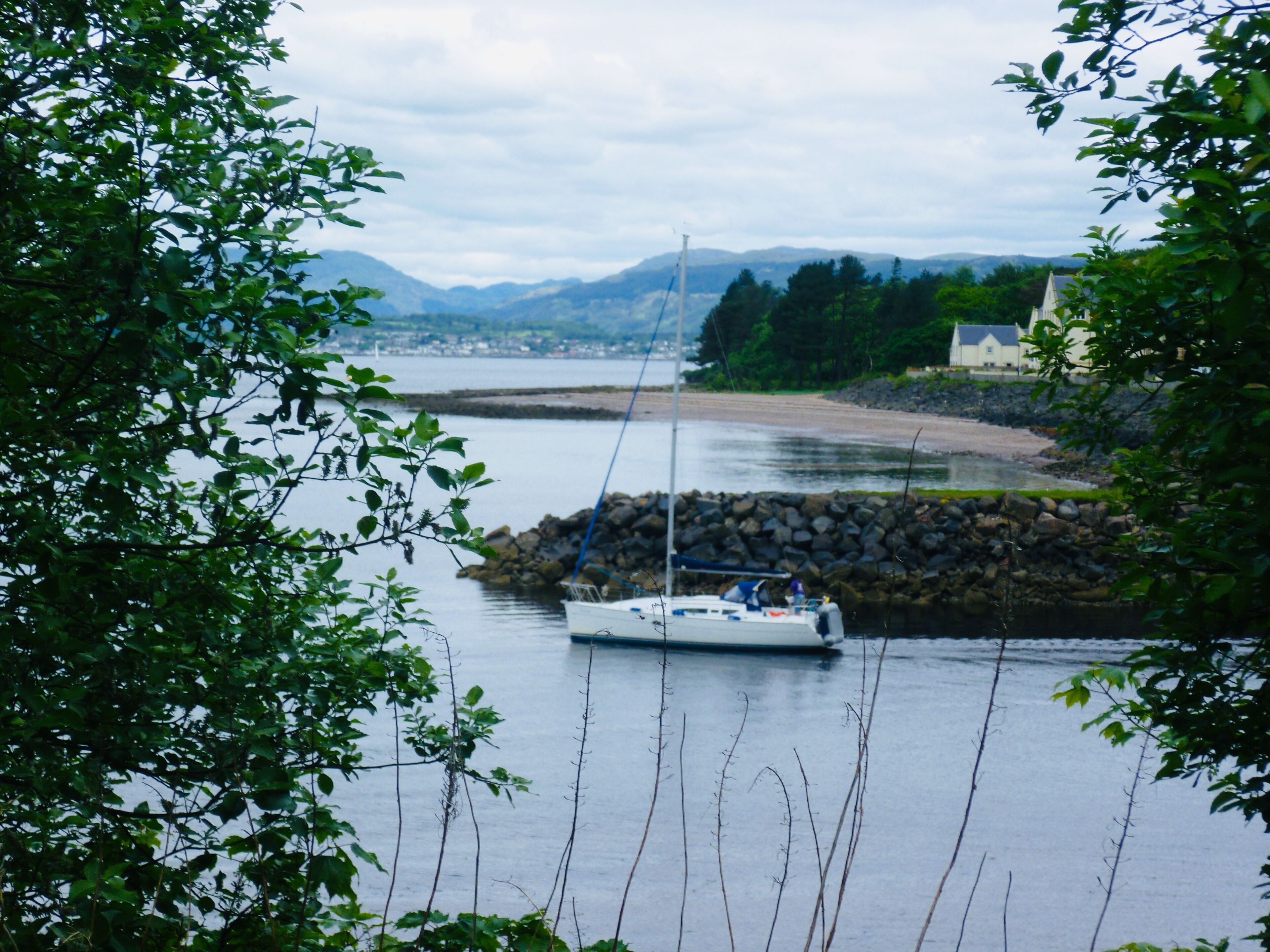 A calm river with a boat docked near a rocky shore, surrounded by greenery and distant mountains.