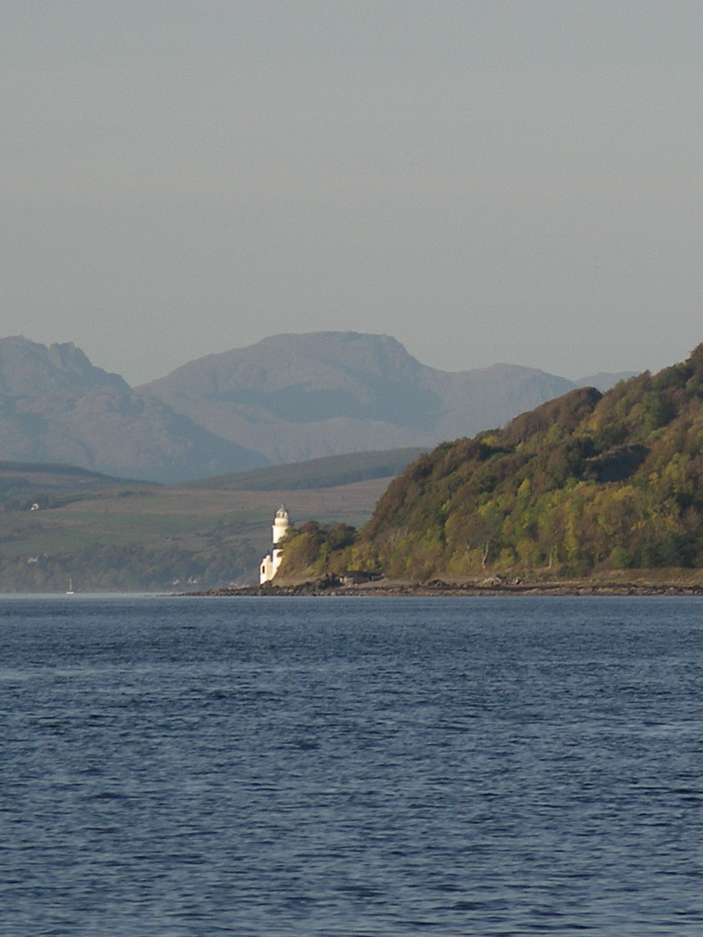 A lighthouse on a rocky coastline with mountains in the background.