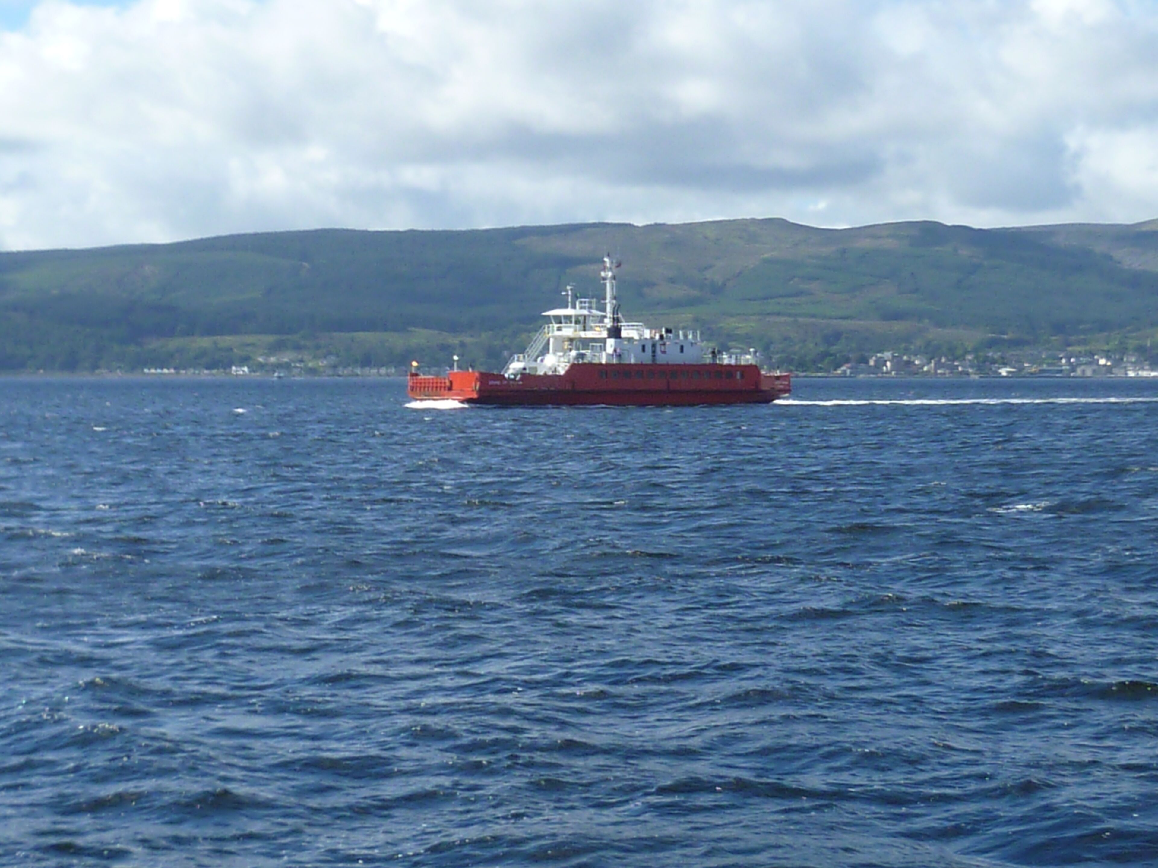 Un barco rojo sobre el agua, con un paisaje montañoso al fondo.