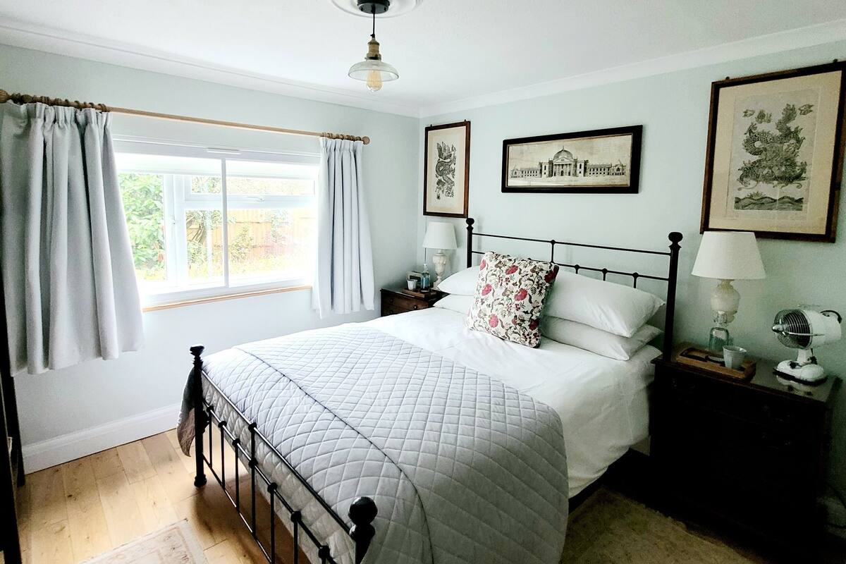 Une chambre à coucher avec un lit, une table de chevet, une lampe et une fenêtre avec des rideaux.