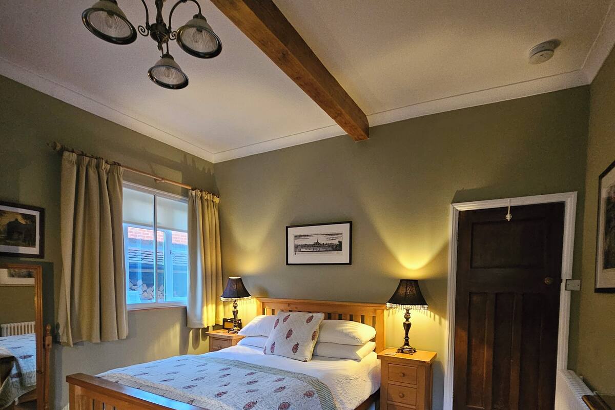 Une chambre à coucher avec un lit en bois, deux tables de chevet avec des lampes, une fenêtre avec des rideaux, une porte et un tableau encadré au mur.