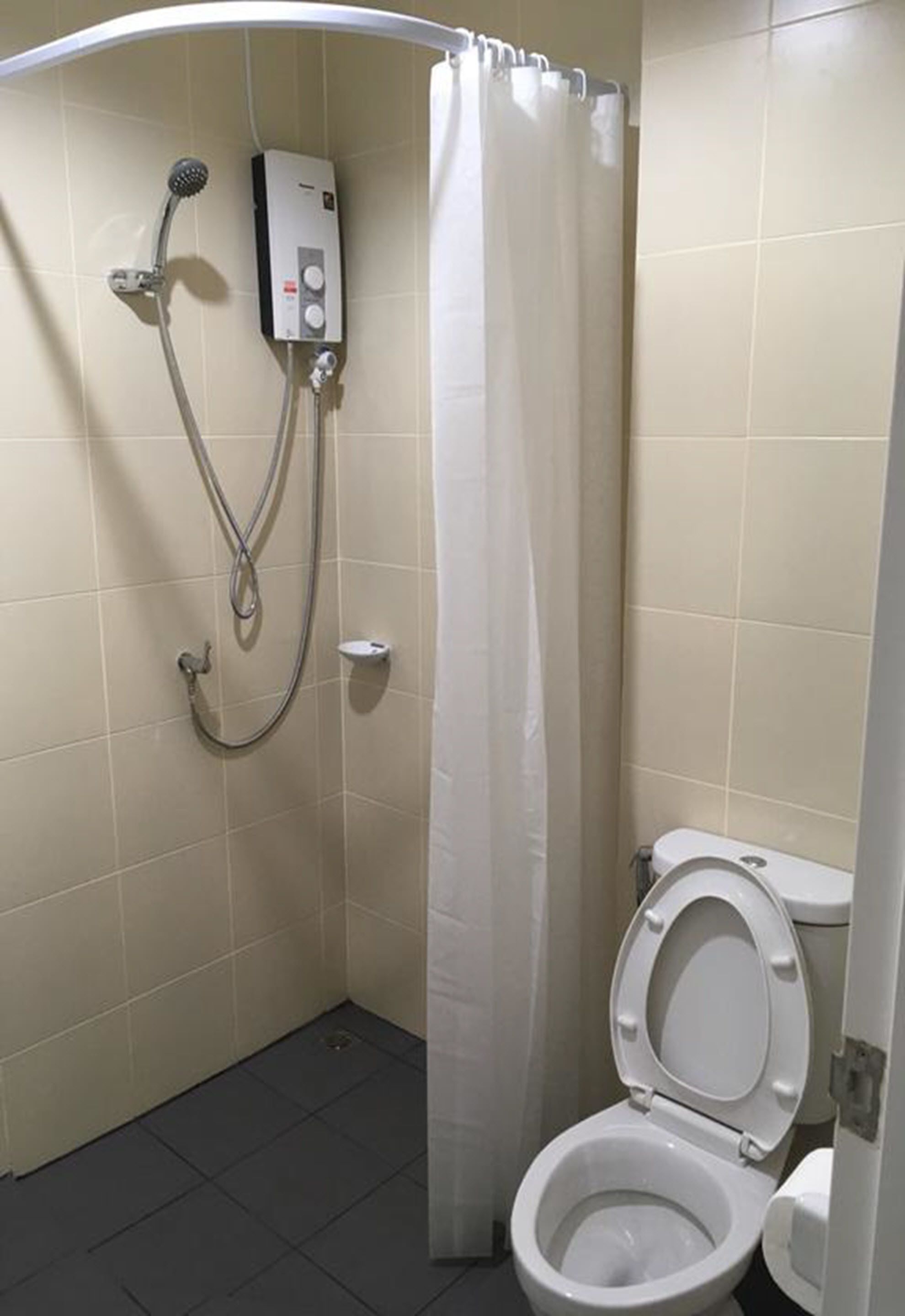A small, enclosed bathroom with a toilet, a shower unit, and a curtain.