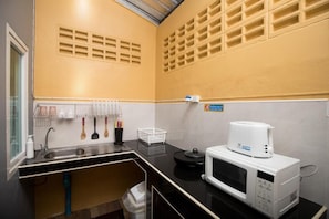 Una cocina compacta con microondas, pileta y un organizador para utensilios.