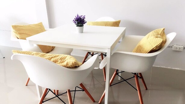 A white dining table with four white chairs, each with a woven cushion. - DKaYa Hostel (Takua Pa)