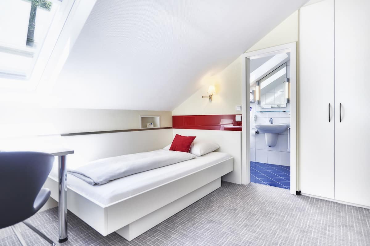 Un dormitorio moderno con cama, escritorio y baño con lavamanos y espejo.