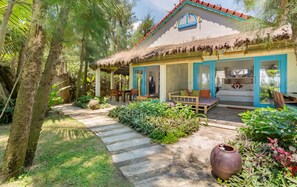 A bungalow with a thatched roof, a dining area, and a bedroom with a bed and a window. - Ocean House (Da Nang)