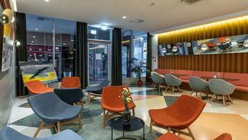 A modern waiting area with colorful chairs, a central table with a vase, and a large mirror wall reflecting the room.