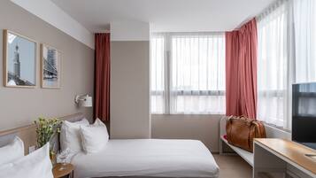 A hotel room with two beds, a TV, a desk, and a window with curtains.