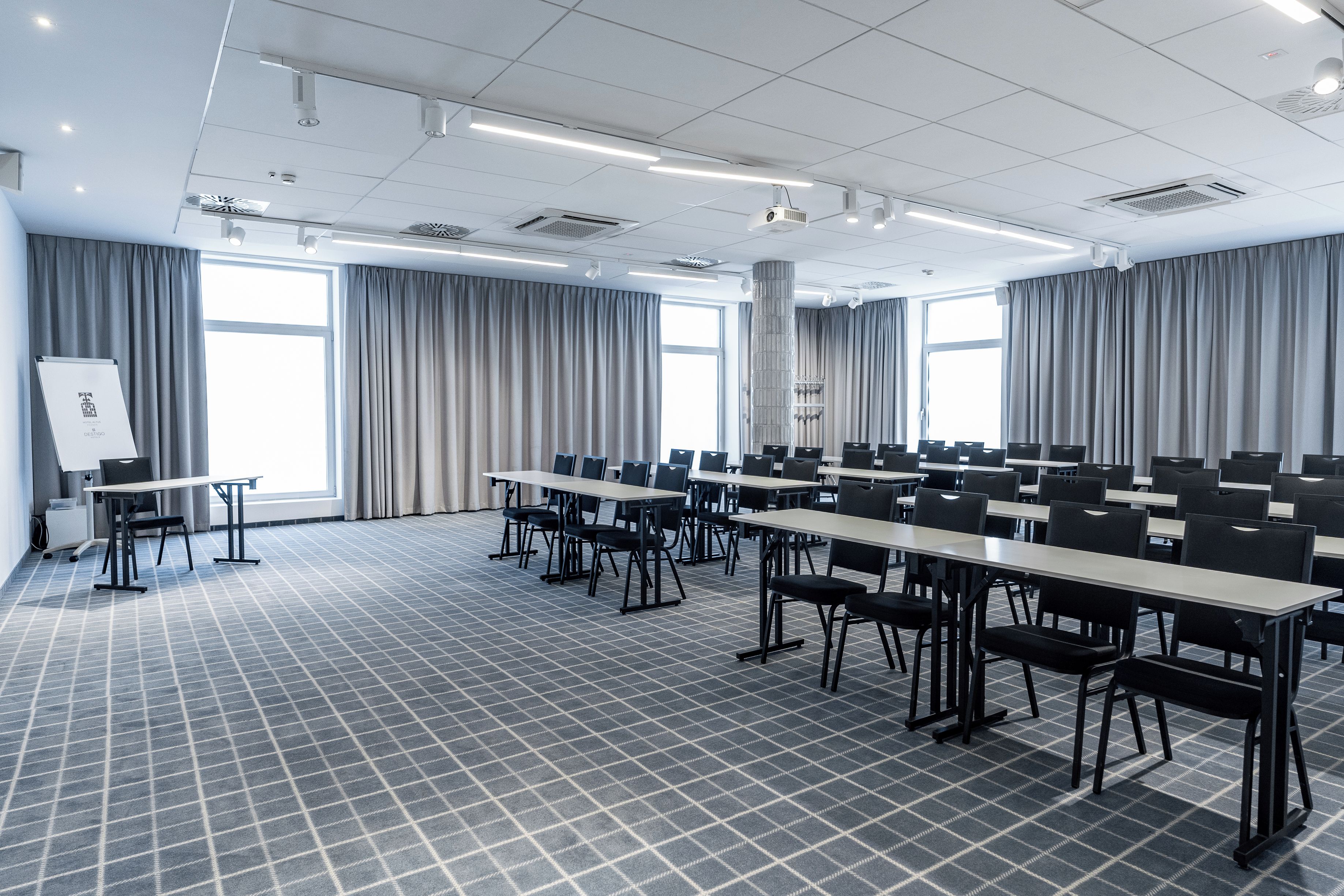 A conference room with a grid-patterned floor, multiple tables, chairs, and large windows with curtains.