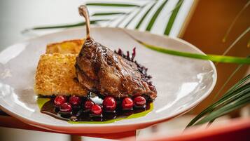 A plate with a roasted duck, a piece of bread, and red berries.